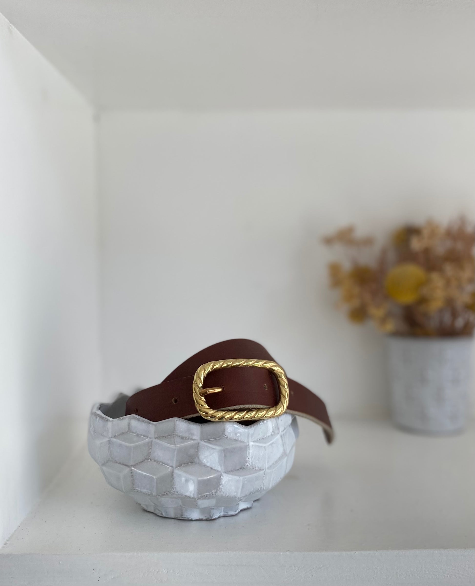 vue d'une ceinture en cuir marron avec une jolie boucle dorée au motif torsadée. Photo prise dans l'atelier traverse à Rennes.