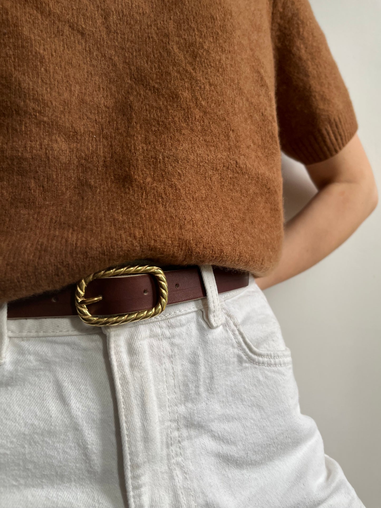 ceinture fine en cuir couleur châtaigne tanné végétalement. La boucle rectangulaire en laiton massif est torsadée. Cette ceinture ets portée sur un jean blanc